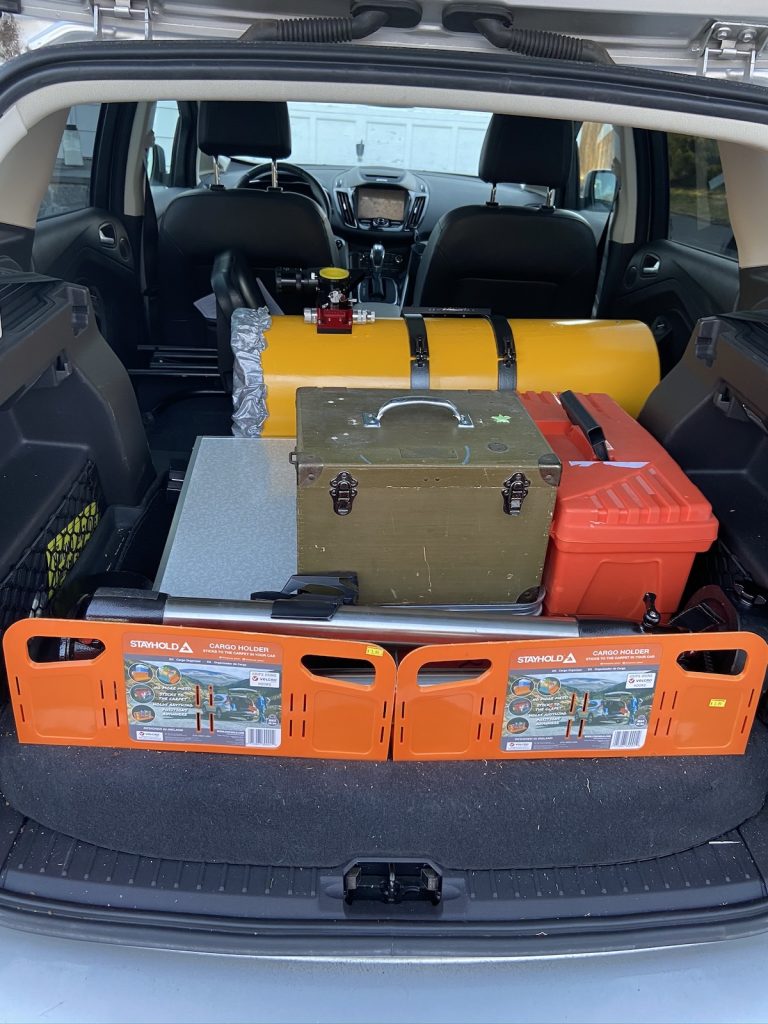 a well-organized car trunk loaded with a yellow Newtonian optical tube and multiple equipment/tool cases